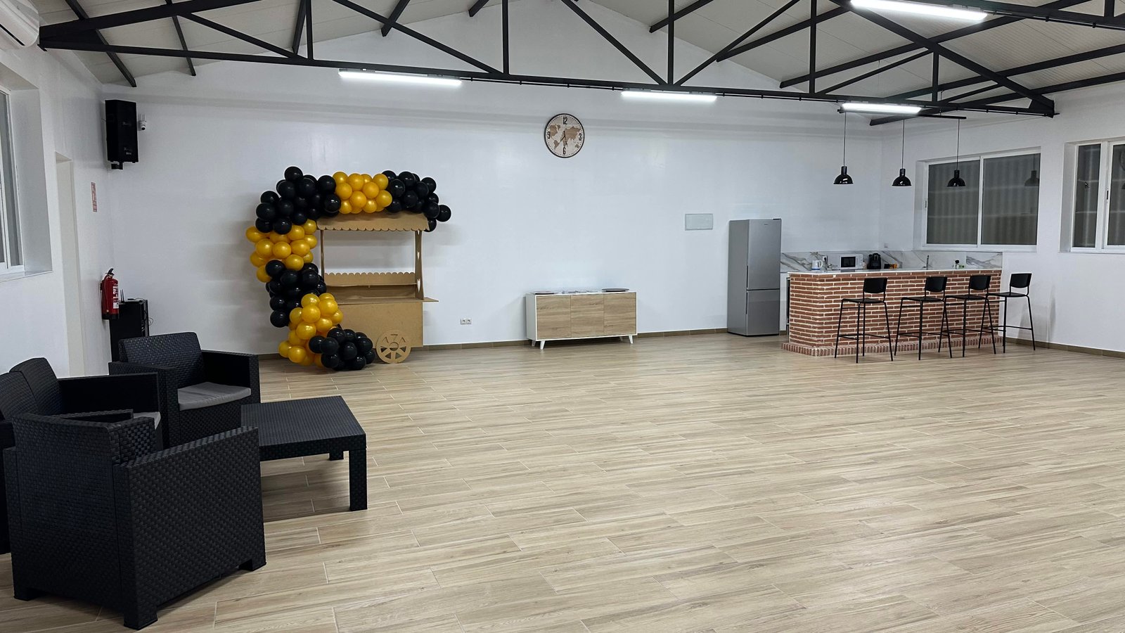 Salón amplio de La Nave con vigas negras, suelo de madera y decoración de globos dorados y negros